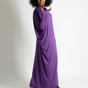 May include: A woman with an afro hairstyle wears a long, purple, flowing dress and holds sunglasses in her hand.