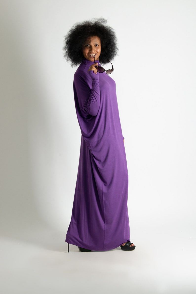May include: A woman with an afro hairstyle wears a long, purple, flowing dress and holds sunglasses in her hand.