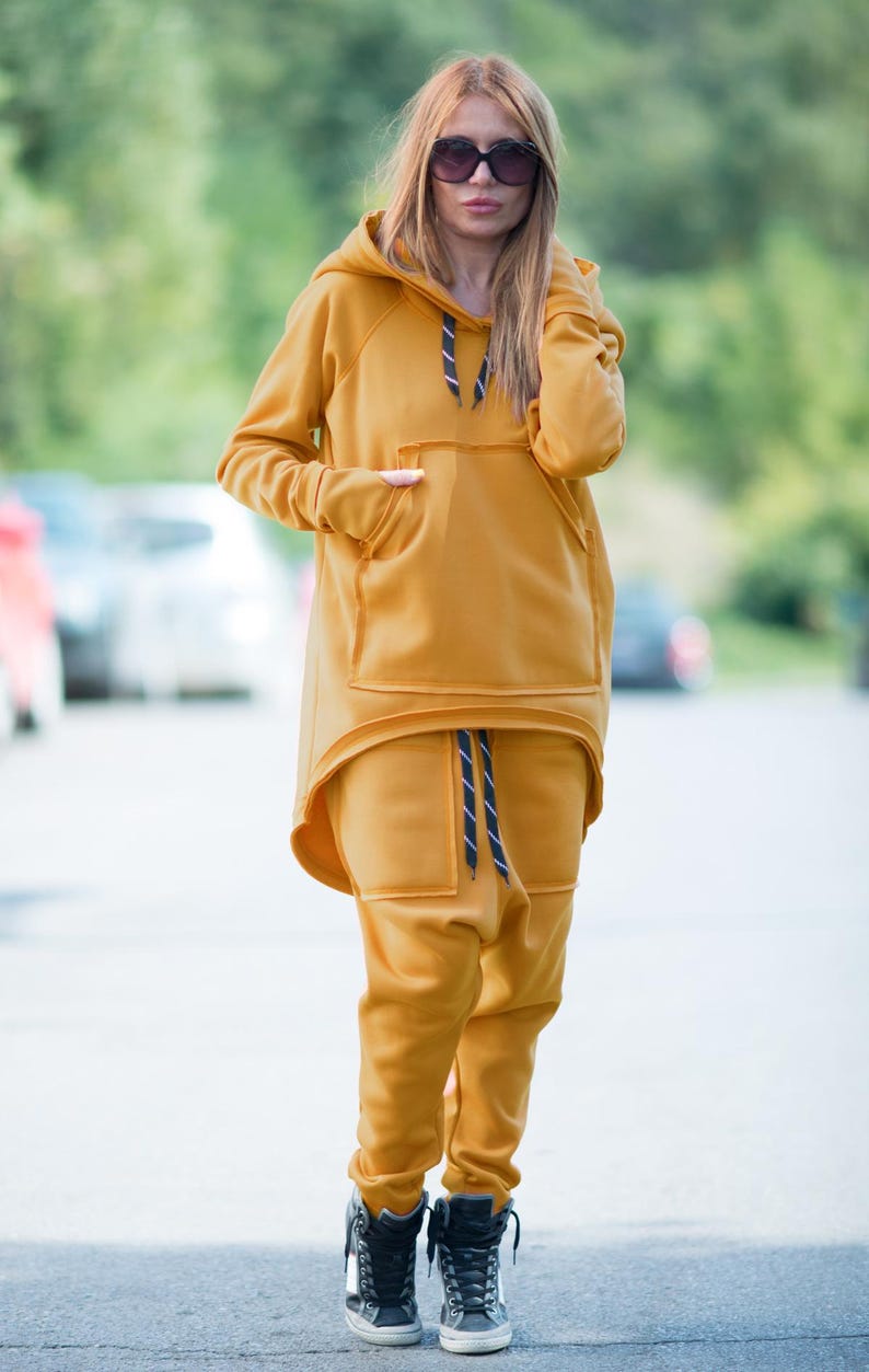 May include: A mustard yellow hooded sweatshirt and matching sweatpants with a black drawstring. The sweatshirt has a large kangaroo pocket and a high-low hemline.