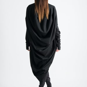 May include: A black long-sleeved dress with a draped design. The dress is fitted at the waist and flows out to the hem. The model is wearing black heels.