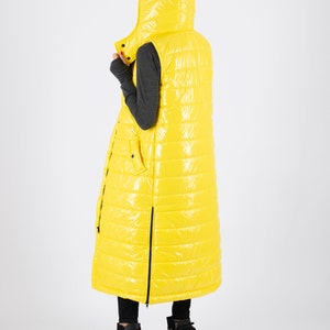 May include: A long yellow puffer vest with a hood. The vest has a zipper down the front and a zippered pocket on the left side.