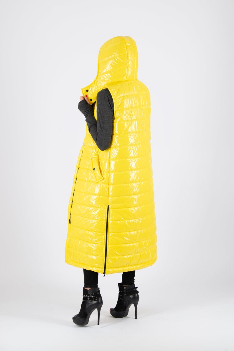 May include: A long yellow puffer vest with a hood. The vest has a zipper down the front and a zippered pocket on the left side.