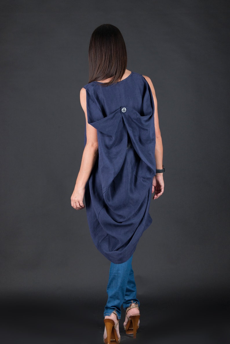 May include: A navy blue sleeveless dress with a gathered back detail and a single button closure. The dress is worn with blue jeans and brown heeled shoes.