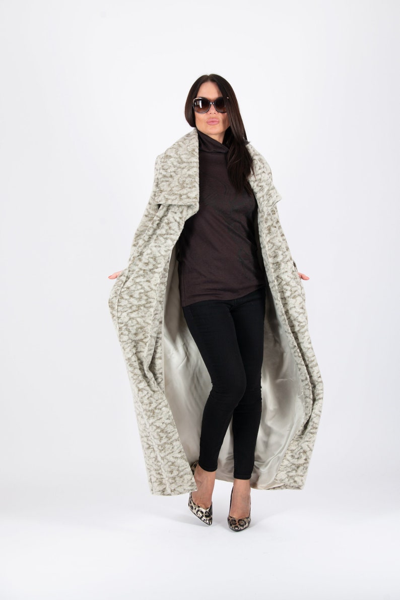 May include: A long, patterned coat in shades of gray and beige, worn over a brown turtleneck and black pants. The coat has a soft, textured appearance. The outfit is completed with patterned heels and sunglasses.
