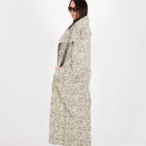 May include: A long, patterned coat in shades of gray and beige. The coat has a shawl collar and pockets. The person is wearing sunglasses and leopard print heels. The coat is floor-length.
