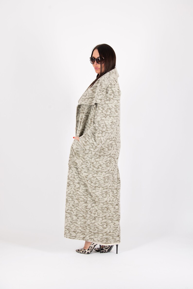 May include: A long, patterned coat in shades of gray and beige. The coat has a shawl collar and pockets. The person is wearing sunglasses and leopard print heels. The coat is floor-length.