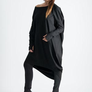May include: A black long-sleeved tunic with a draped design and a wide neckline. The tunic is worn with black leggings and black high-heeled shoes.