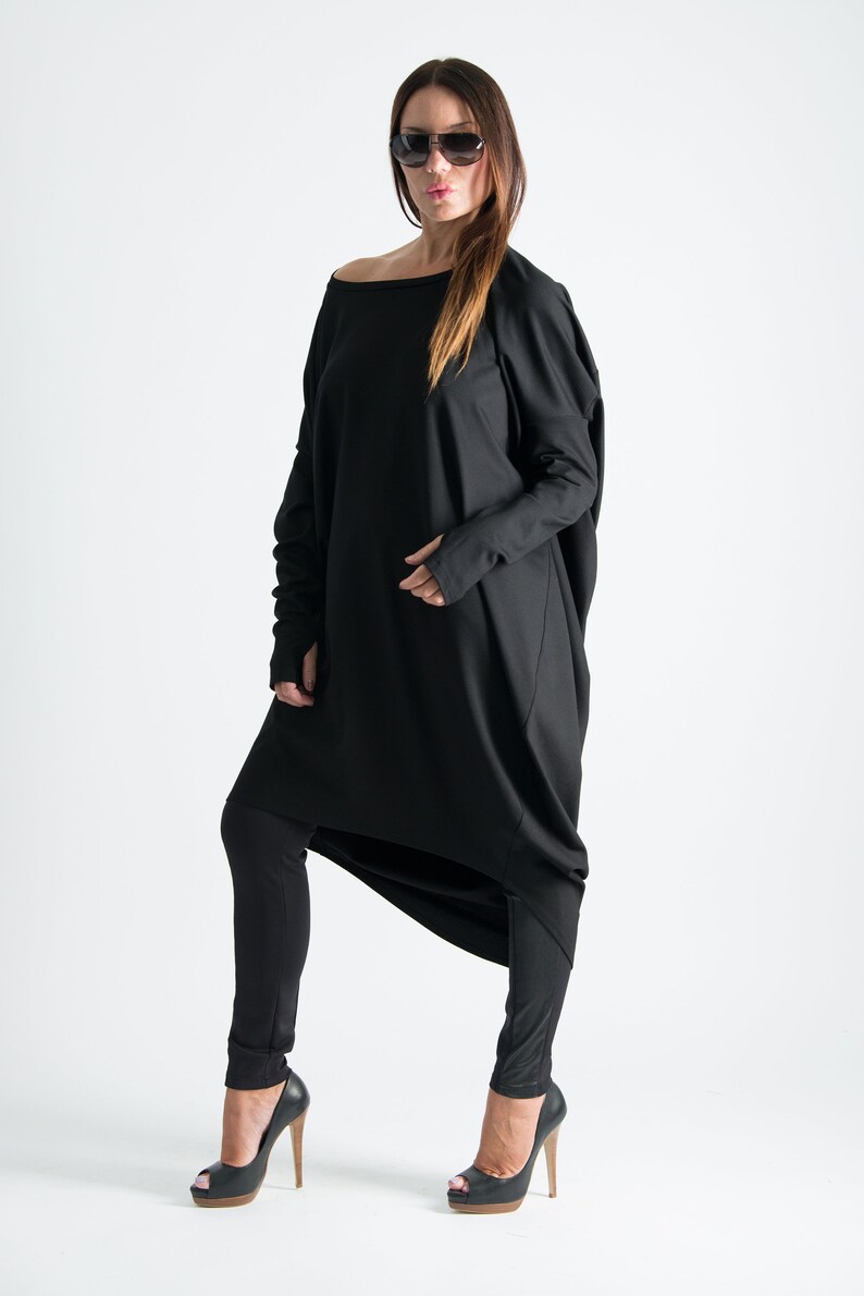May include: A black long-sleeved tunic with a draped design and a wide neckline. The tunic is worn with black leggings and black high-heeled shoes.