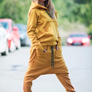 May include: A mustard yellow hooded sweatshirt and matching sweatpants with a drawstring waist. The outfit is made of a soft, comfortable fabric and features a relaxed fit.