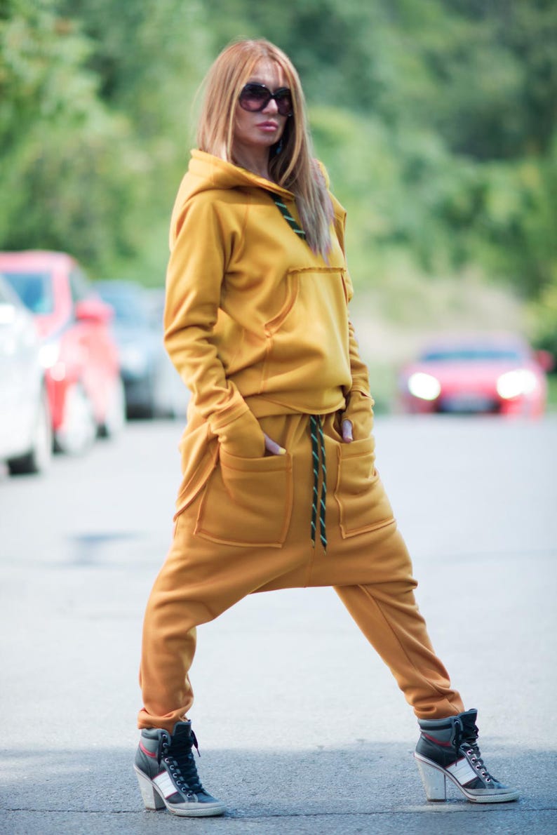 May include: A mustard yellow hooded sweatshirt and matching sweatpants with a drawstring waist. The outfit is made of a soft, comfortable fabric and features a relaxed fit.