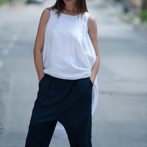 May include: A woman wearing a white linen top with a loose, flowing silhouette and dark blue, cropped, wide-leg pants. She is wearing sunglasses and white heeled sandals.