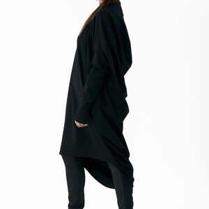 May include: A black long-sleeved tunic with a high neckline and a draped design. The tunic is worn with black leggings and black high-heeled shoes.