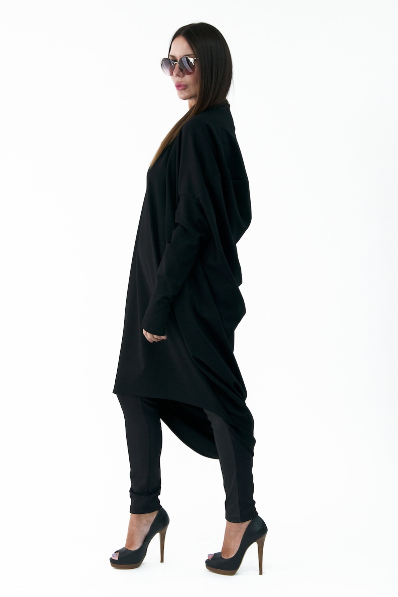 May include: A black long-sleeved tunic with a high neckline and a draped design. The tunic is worn with black leggings and black high-heeled shoes.