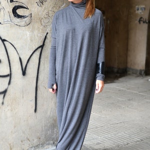 May include: A gray long-sleeved maxi dress with a turtleneck and a black leather cuff on the left sleeve. The dress is made of a soft, stretchy fabric and has a relaxed fit.