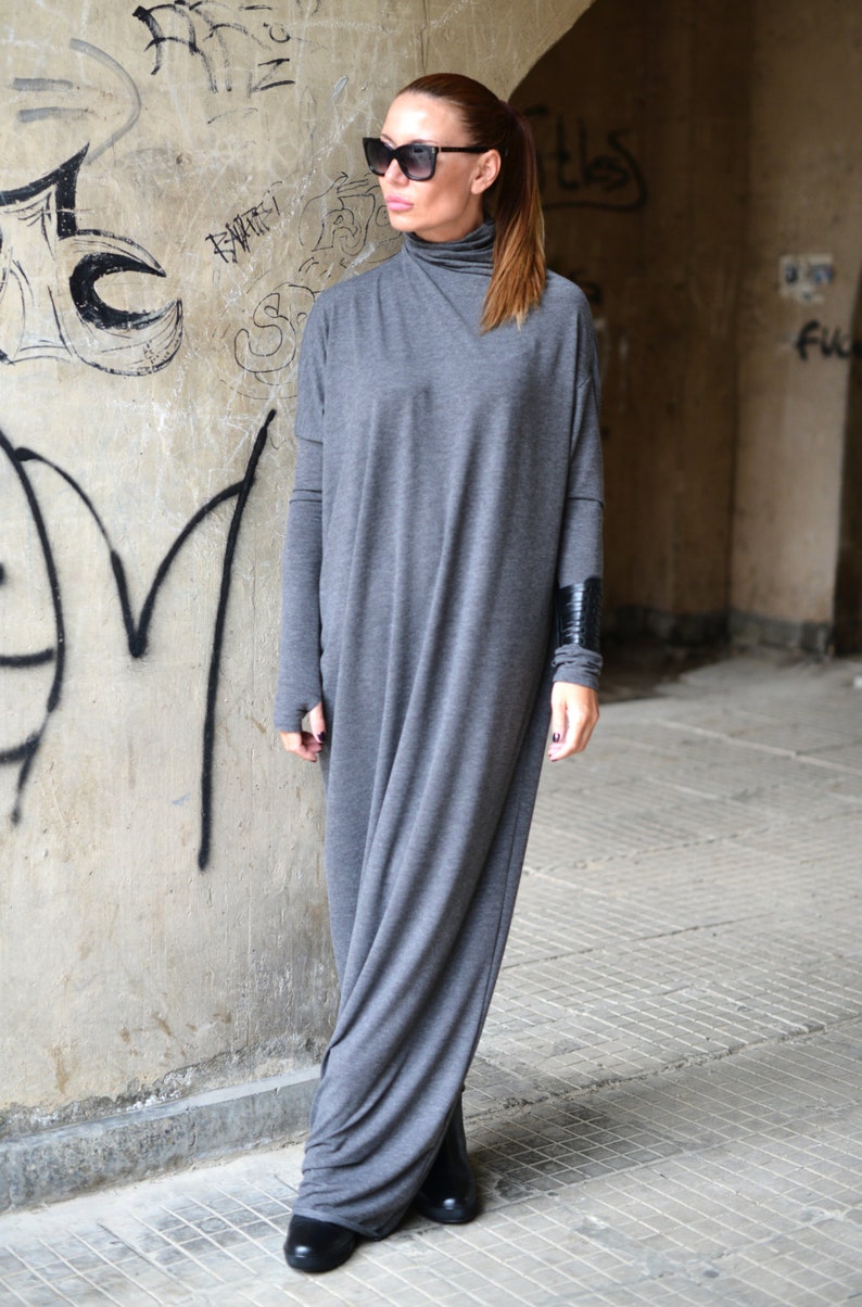 May include: A gray long-sleeved maxi dress with a turtleneck and a black leather cuff on the left sleeve. The dress is made of a soft, stretchy fabric and has a relaxed fit.