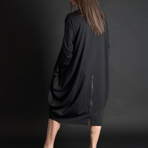 May include: A black long-sleeved dress with a zipper down the back. The dress is loose-fitting and has a gathered look. The model is wearing black high-heeled sandals.