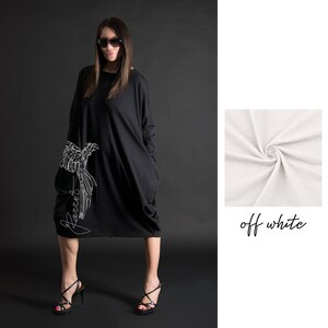 May include: Black oversized dress with a white parrot graphic and the word "Parrots" written vertically on the side. The dress has long sleeves and large pockets. The model is wearing black heels.