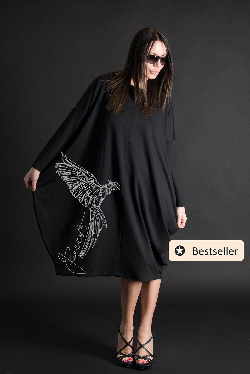 May include: Black oversized dress with a white parrot graphic and the word "Parrot" written in cursive. The dress is knee-length and has a loose fit. The model is wearing black heels.