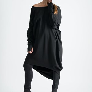 May include: A black long-sleeved tunic with a draped design, worn with black leggings and black peep-toe heels.