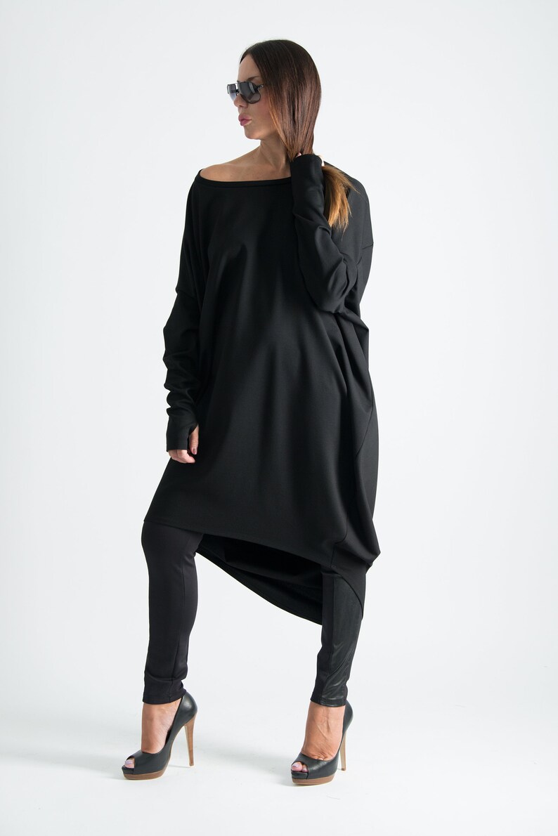 May include: A black long-sleeved tunic with a draped design, worn with black leggings and black peep-toe heels.