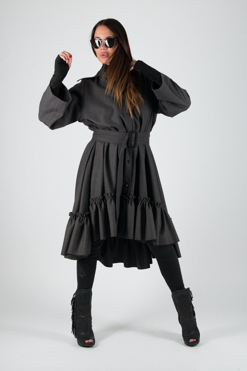 May include: A charcoal gray dress with a high collar, long sleeves, and a belted waist. The dress features a ruffled hemline and is paired with black leggings and open-toe boots with fringe.