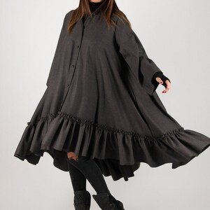 May include: A dark gray, button-down dress with a ruffled hem. The dress has long sleeves and a high-low design. The model is wearing black sunglasses and black boots.