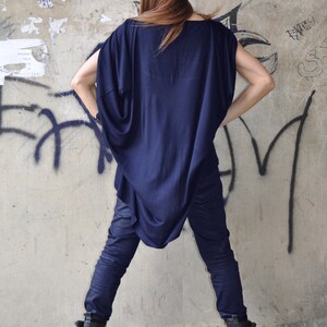 May include: A woman wearing a navy blue, loose-fitting top with a long, flowing design. She is also wearing dark blue jeans and black boots with buckles.