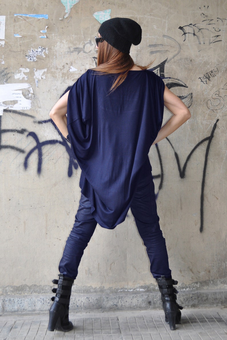 May include: A woman wearing a navy blue, loose-fitting top with a long, flowing design. She is also wearing dark blue jeans and black boots with buckles.