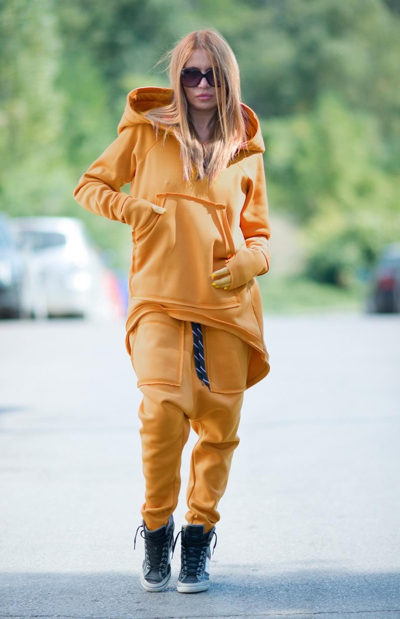 May include: A mustard yellow hooded sweatshirt and matching sweatpants with a black and white striped belt. The sweatshirt has a large kangaroo pocket and the sweatpants have a loose, baggy fit.