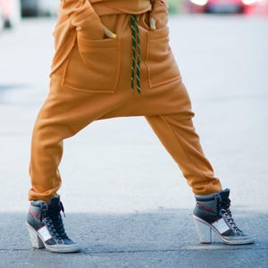 May include: A pair of mustard yellow sweatpants with a green drawstring and large pockets. The sweatpants are styled with a loose fit and are worn with black high-top sneakers.