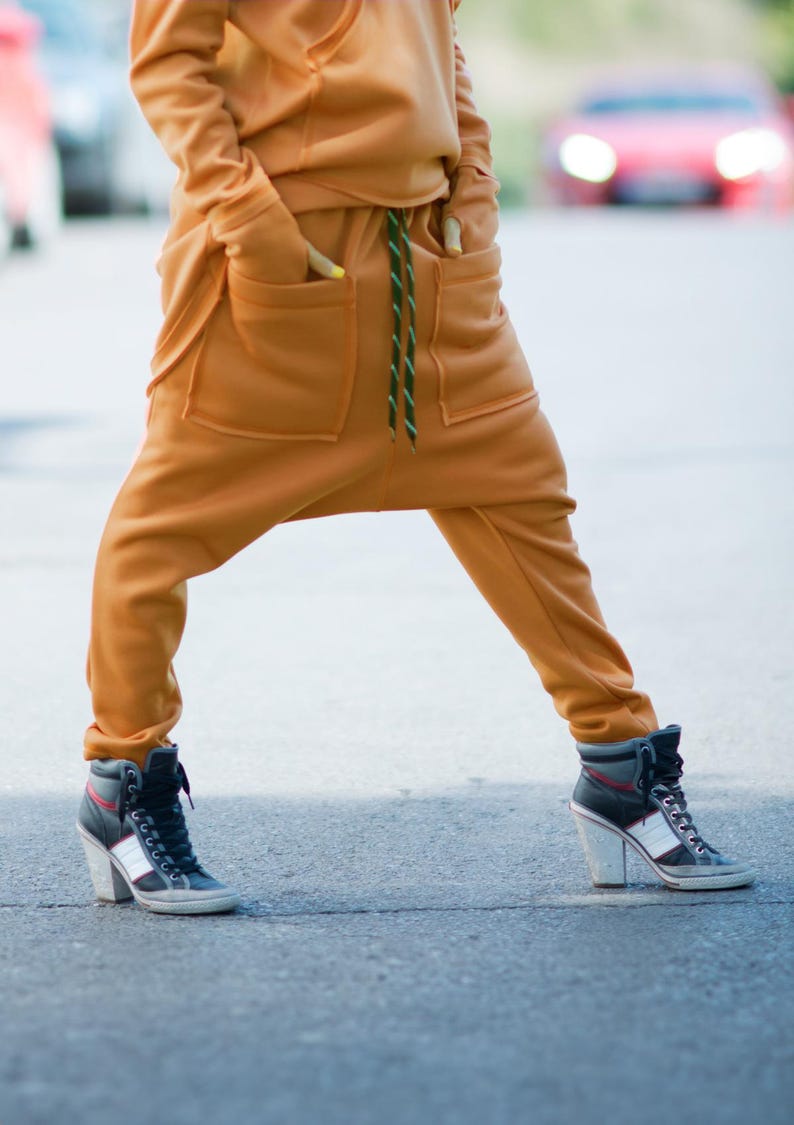 May include: A pair of mustard yellow sweatpants with a green drawstring and large pockets. The sweatpants are styled with a loose fit and are worn with black high-top sneakers.