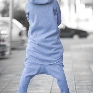 May include: A person wearing a light blue hooded sweatshirt and matching sweatpants. The person is standing on a brick walkway.