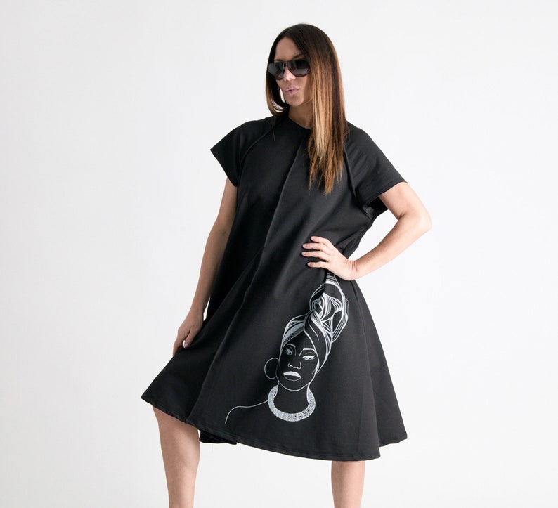 May include: A black short-sleeved dress with a white line drawing of a woman's face on the side. The woman is wearing a headscarf.