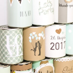 May include: A stack of decorated cans with various designs, including hearts, balloons, and the words "Love", "Let's Party", "Wunderpaar", "26. August 2017", and "Dose Glück".