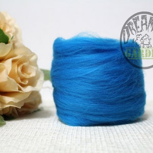 May include: A close-up of a bright blue wool roving, a type of fibre used for felting and spinning. The roving is rolled up and is sitting on a white surface. The text "Dreamer Garden" is visible in the background.