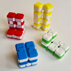 Puede incluir: Cuatro juguetes antiestrés de diferentes colores: rojo, amarillo, azul y verde. Cada juguete está hecho de plástico y tiene un diseño único. Los juguetes son todos de forma cuadrada y tienen una franja blanca alrededor del medio.