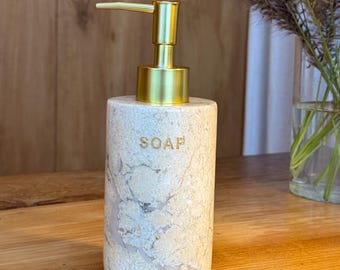 Dispensador de mármol para jabón con bomba dorada. Decoración minimalista para el baño. Baño moderno y elegante.
