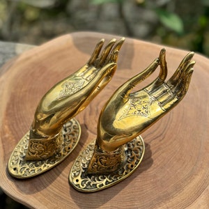 Puede incluir: Un par de tiradores de puerta de latón adornados con forma de manos en posición de oración. Los tiradores tienen detalles intrincados y están montados sobre bases ovaladas.