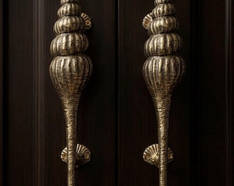 May include: Two ornate, brass-colored door handles. Each handle is shaped like a stylized seashell, with a spiraling top and a long, textured stem. They are mounted on a dark brown wooden door.