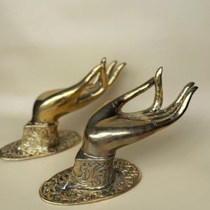 Puede incluir: Dos tiradores de puerta de latón adornados con forma de manos en un gesto de oración o bendición. Los tiradores están detallados con intrincados patrones florales.