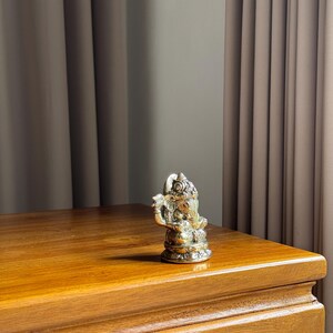 May include: A silver Ganesha statue with intricate details sits on a wooden table. The statue is about 5 inches tall and has a trunk pointing to the right.