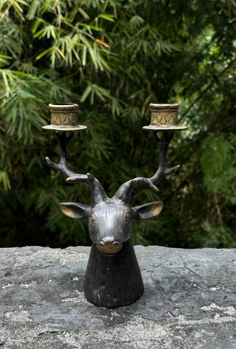 May include: A black metal deer head candle holder with two gold candle cups. The deer head is detailed with antlers and a realistic face.