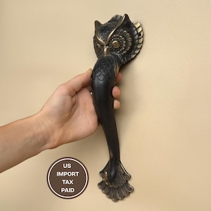 以下が含まれることがあります： ブロンズ調のフクロウ型のドアハンドル。ハンドルは上部にフクロウの頭部、長く湾曲したボディが特徴です。ハンドルは手で持たれています。「US IMPORT TAX PAID」の文字が円で囲まれています。