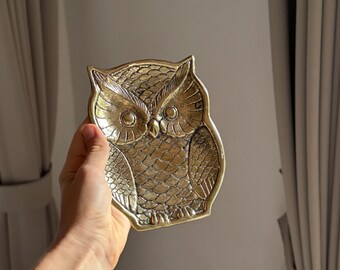 May include: A gold-colored metal owl-shaped trinket dish. The owl has detailed features and a textured surface.