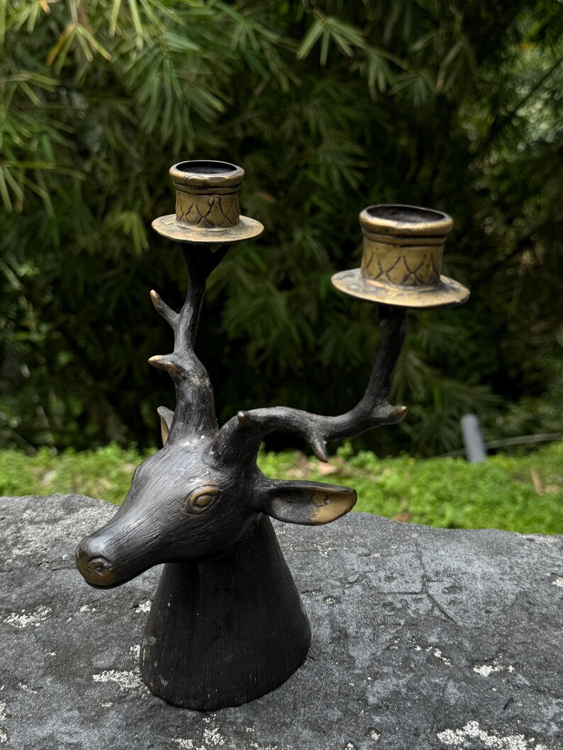 May include: A black metal deer head candle holder with two gold candle cups. The deer head has a detailed design and the candle cups have a geometric pattern.