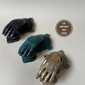 May include: Three decorative hand-shaped door knockers in black, teal, and gold. Each knocker features a detailed hand design with a decorative backplate. The knockers are made of metal and have a vintage aesthetic.