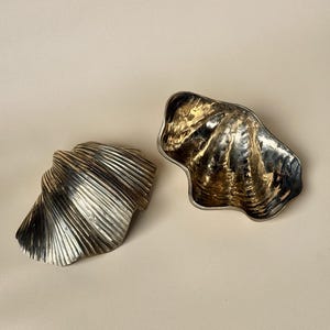 以下が含まれることがあります： 金色の金属製の貝殻の形をした装飾的なボウル2つ。ボウルはサイズが異なり、表面がテクスチャ加工されています。