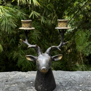 May include: A black metal deer head candle holder with two gold candle cups. The deer head is detailed with antlers and a realistic face.