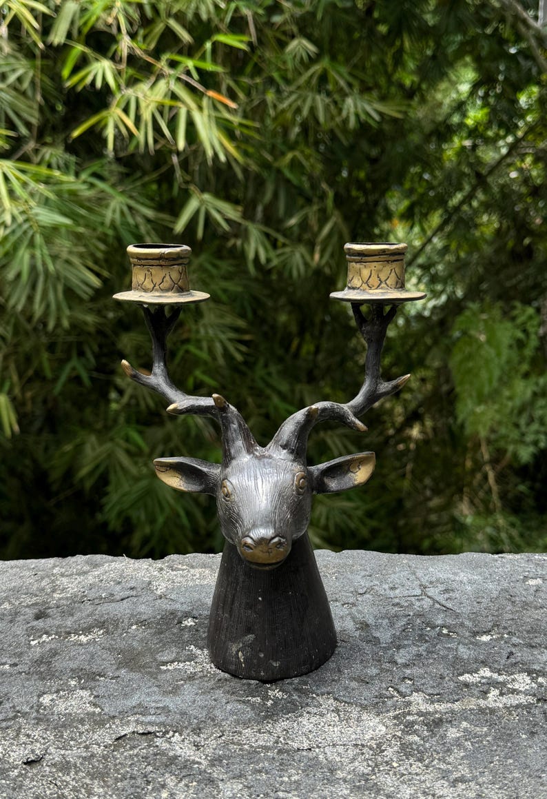 May include: A black metal deer head candle holder with two gold candle cups. The deer head is detailed with antlers and a realistic face.