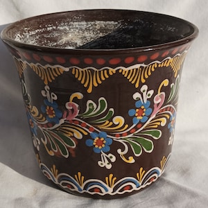 May include: A brown ceramic planter with a floral design. The design features blue, pink, yellow, and green flowers and leaves. The planter has a slightly flared rim.